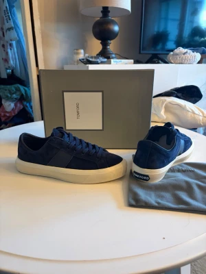 Tom Ford skor - Snygga sneakers från Tom Ford i mörkblå mocka med vit sula och klassisk låg profil. Skorna har diskret branding på hälen och matchande blåa skosnören. Perfekt för dig som vill ha en stilren och exklusiv look.