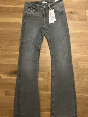 Grå bootcut jeans från Lee - Snygga grå bootcut jeans från Lee med klassisk femficksdesign och knappar på bakfickorna. Jeansen har en lätt tvättad look och är tillverkade i bomull. Perfekta för dig som gillar en avslappnad och trendig stil.