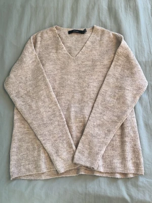 Beige ribbstickad tröja V-ringning - Mjuk och ribbstickad beige tröja från Vero Moda med V-ringning och långa ärmar. Perfekt för lager-på-lager och enkel att matcha med jeans eller kjol. Materialet är troligtvis en blandning av syntet och ull för extra komfort.