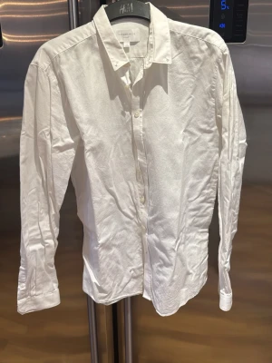 Vit skjorta från Lindbergh - Klassisk vit skjorta från Lindbergh i storlek M. Skjortan har lång ärm, knappar framtill och en stilren krage. Perfekt för dig som vill ha en enkel och snygg skjorta till garderoben. Materialet är bomull och modellen har normal passning.