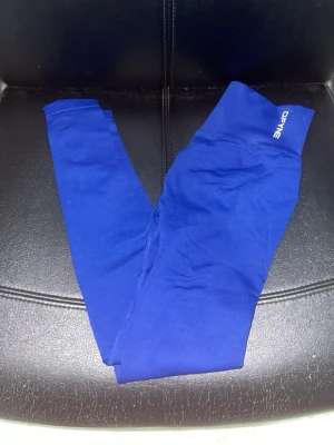 Blå leggings från DFYNE - Snygga blå leggings från DFYNE med hög midja och scrunch-detalj bak. Perfekta för träning eller chill. Materialet är stretchigt och följsamt, vilket ger en bekväm passform och framhäver formen. Logotypen är tryckt på midjan.