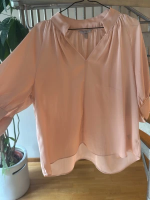 Ljusrosa blus med v-ringning - Säljer en ljusrosa blus med v-ringning och trekvartsärm. Blusen har en lös passform och är tillverkad i ett tunt, flowy material som ger en snygg siluett. Perfekt för dig som gillar stilrena och feminina plagg.