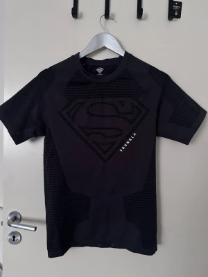 Svart Superman t-shirt från YoungLA - Snygg svart t-shirt från YoungLA med stort Superman-logga på bröstet. T-shirten har korta ärmar och coola strukturerade paneler på axlar och sidor. Perfekt för dig som gillar superhjältar och streetwear. Aldrig använt den! Priset kan diskuteras