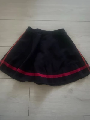 Arket marinblå kortkjol med röd rand - Snygg marinblå kortkjol med en röd rand längs nederkanten och sidorna. Materialet känns mjukt och följsamt. Jag har inte använt kjolen med tyvärr ingen prislapp kvar.💕