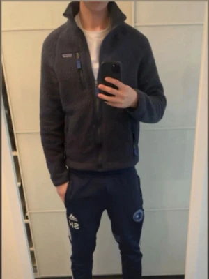 Svart fleecejacka från Patagonia - Mysig svart fleecejacka från Patagonia med hög krage och dragkedja framtill. Jackan är i bra skick men har en liten deflekt på högra armen, som syns på bilden.