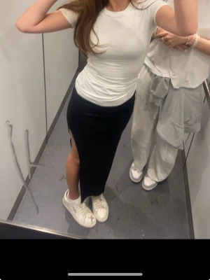 Svart långkjol med slits från Bershka - Säljer en svart långkjol från Bershka med en snygg slits på sidan. Kjolen har en enkel och stilren design som passar perfekt till sneakers eller klackar. Materialet är mjukt och följsamt för en bekväm passform.