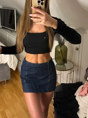 Mörkblå jeanskjol i kort modell - Trendig mörkblå jeanskjol i kort modell med synliga sömmar framtill. Kjolen har en klassisk, rak passform och är perfekt att matcha med crop tops eller stickade tröjor. Inga fickor eller extra detaljer, enkel och stilren design.