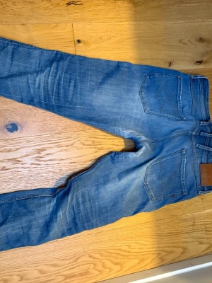 Blå jeans från Replay Anbass - Säljer ett par blå jeans från Replay, modell Anbass. Jeansen har klassisk femficksdesign, raka ben och snygga slitningar för en avslappnad look. Tillverkade i bomull med en skön passform. Perfekta för dig som gillar stilrena och trendiga jeans.