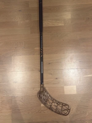 Innebandyklubba Oxdog svart/brons - Säljer en innebandyklubba från Oxdog med svart skaft och bronsfärgat blad. Klubban har ett stilrent utseende med tydlig Oxdog-logga på skaftet och ett lätt, hålat blad i plast. Perfekt för dig som gillar innebandy och vill ha en snygg klubba. Helt ny med minimal slitage 