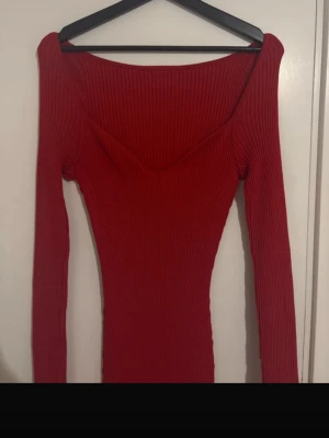 Röd ribbad långklänning - Snygg röd långklänning med ribbad struktur och v-ringad urringning. Klänningen har lång ärm och figurnära passform som framhäver siluetten. Perfekt för dig som vill sticka ut med en enkel men trendig look.