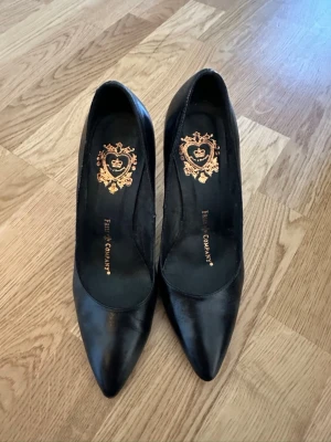 Svarta pumps från Friis & Company stl 39 - Klassiska svarta pumps i skinn från Friis & Company med spetsig tå och medelhög klack 9 cm. Snygg gulddetalj med logga på innersulan. Perfekta för dig som gillar stilrena och tidlösa skor.