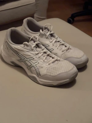 Vita inomhus tränings skor, Asics sneakers - Snygga vita Gel rocket 11, sneakers från Asics med klassiska silverfärgade detaljer på sidorna. Skorna har mesh- och syntetmaterial för bra andningsförmåga och komfort. Perfekta för dig som gillar sportig stil och vill ha ett par lätta och bekväma sneakers, som även funkar perfekt för inomhusträning.
