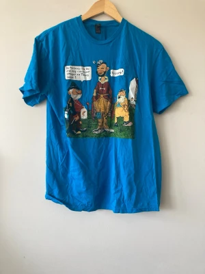 Blå t-shirt med tecknad print 💚 - Cool T-shirt med tecknad print i storlek L men jag skulle säga lite liten i storleken . 