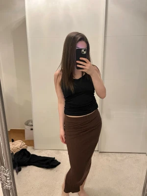 Brun ribbad långkjol - Säljer en brun långkjol med ribbad struktur. Kjolen har en enkel och stilren design med elastisk midja och smal passform som framhäver siluetten. Perfekt för dig som gillar en avslappnad men trendig look.