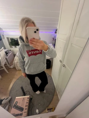Grå Levi's hoodie med röd logga - Säljer en grå hoodie från Levi's med den klassiska röda loggan framtill. Hoodien har huva med dragsko och är tillverkad i mjukt sweatshirtmaterial. 