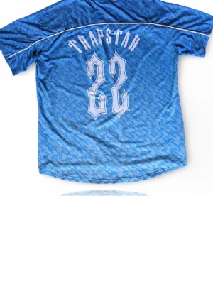 Blå Trapstar t-shirt med mönster - Säljer en blå t-shirt från Trapstar med all-over mönster och tryck både fram och bak. Framsidan har Trapstar-logga och texten 'It’s a sport', medan baksidan har stort nummer 22. T-shirten har rund hals och korta ärmar, perfekt för en streetwear-look.