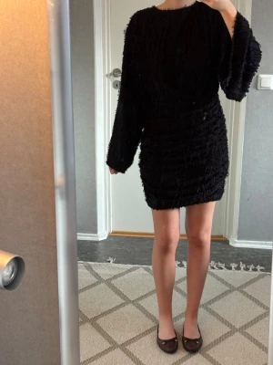 Svart kort klänning med öppen rygg - Säljer en svart kort klänning med vida långärmar. Klänningen har en snygg öppen rygg med knyt upptill och en figurnära passform. Endast använd 1 gång. 