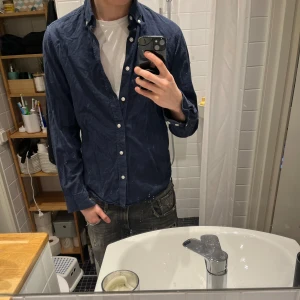 Mörkblå skjorta från Dobber - Mörkblå skjorta från Dobber i klassisk modell med knappar framtill och krage. Skjortan är långärmad och har en avslappnad passform, perfekt att bära över en t-shirt. Tillverkad i mjuk bomull för en bekväm känsla.