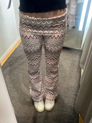 Mjukisbyxor med zigzag-mönster - Säljer ett par mjukisbyxor med snyggt zigzag-mönster i rosa, vitt och svart. Byxorna har utsvängda ben och bred linning för extra komfort. Perfekta för dig som gillar färg och mönster i din vardagsstil. Storlek 170 passar xs/s!