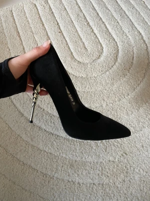 Svarta pumps med guldfärgad klack - Snygga svarta pumps med spetsig tå och guldfärgad smal klack. Skorna har en klassisk siluett, perfekta för dig som vill ha en elegant och trendig look.