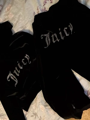 Svart velourset från Juicy Couture - Säljer ett svart velourset från Juicy Couture med glittrande texten 'Juicy' i strass på ryggen. Setet består av en ziptröja och matchande byxor, perfekt för en avslappnad och trendig look hemma.