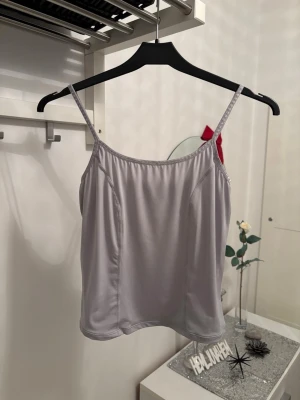 Ljusgrå linnetopp med smala axelband - Säljer en enkel och stilren ljusgrå linnetopp med smala axelband. Toppen har en rak passform och är tillverkad i ett mjukt, stretchigt syntetmaterial som känns skönt mot huden. Perfekt att matcha med jeans eller kjol för en clean look.