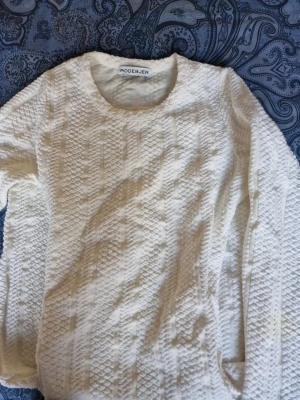 Vit klänning från Rodebjer - Säljer en vit stickad tröja från Rodebjer med rund halsringning och lång ärm. Tröjan har ett strukturerat, rutigt mönster i stickningen som ger en snygg och modern look. Perfekt att styla till jeans eller kjol för en clean outfit.