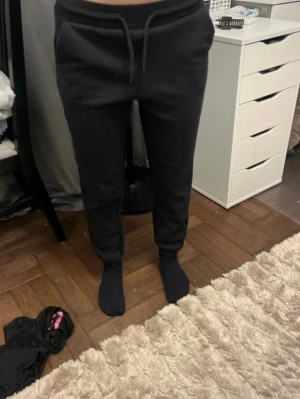 Svarta mjukisbyxor med dragsko - Säljer ett par svarta mjukisbyxor med dragsko i midjan och smal passform. Byxorna har muddar vid bensluten och är tillverkade i ett mjukt och bekvämt material, perfekta för chill dagar hemma eller när du vill vara extra comfy.
