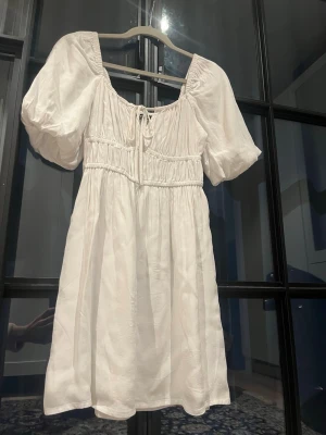 Vit kort klänning med puffärm - Supersöt vit kortklänning perfekt till studenten! Använd 1 gång på en skolavslutning. Den har  puffärmar och knyt vid brösten. snöret går att dra åt och justera till önskad storlek. Ärmarna kan man också justera lite vart man vill att de ska sluta på armen. Klänningen har smock i midjan för en snygg passform och är tillverkad i ett mjukt, lätt tyg som känns perfekt för varmare dagar. Den har 2 lager tyg så jag tycker inte den blir genomskinlig.