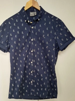 Mörkblå skjorta med mönster från ASOS - Kortärmad skjorta från ASOS i mörkblått med små vita blommiga mönster över hela.