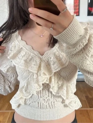 Vit virkad volangtröja - Supersöt vit stickad tröja med volanger och virkat mönster. Tröjan har långa ärmar, bred mudd i midjan och en croppad passform. Perfekt för dig som gillar romantisk och trendig stil. Materialet känns mjukt och luftigt.
