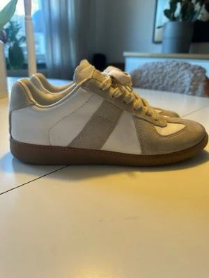 Gats  - Gats i vitt och beige med ovandel i lammnappa och kalvskinn. Klassisk låg modell med gummisula och snörning. Perfekta för dig som gillar minimalistisk och stilren design.