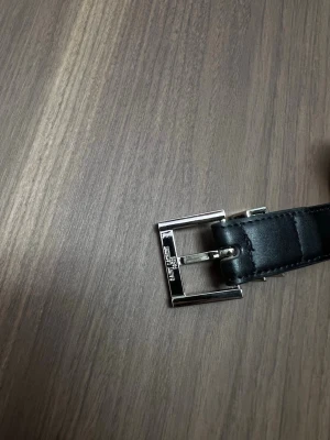 Svart bälte från Saint Laurent - Snyggt svart bälte från Saint Laurent i skinn med klassiskt silverfärgat spänne och YSL-detalj. Perfekt accessoar för att lyfta vilken outfit som helst. Enkel och stilren design med exklusiv känsla.