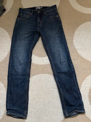Mörkblå raka jeans - Säljer ett par klassiska mörkblå jeans med raka ben och fem fickor. Jeansen har snygga slitningar och kontrastsömmar. Perfekta till vardagslooken och passar till det mesta. Materialet är denim i bomull.W28 L32