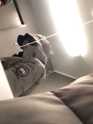 Svart pufferjacka från Canada Goose  - Canada Goose pufferjacka i svart med huva och avtagbar fuskpäls. Jackan har dragkedja och knappar framtill, två sidofickor och ribbade muddar vid ärmslut. Märkespatch på ärmen och quiltad design för extra värme. Perfekt för kalla vinterdagar.