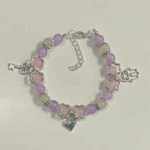 Lila och rosa pärlarmband med berlocker - HANDGJORT armband med lila, rosa och vita pärlor samt silverfärgade detaljer. Armbandet har silverfärgade berlocker. Justerbar kedja för perfekt passform.