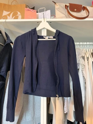 Mörkblå kofta från Gina Tricot - Mörkblå hoodie från Gina Tricot med dragkedja framtill och huva. Modellen är rak och har långa ärmar samt ribbade muddar vid ärmslut och nederkant. 
