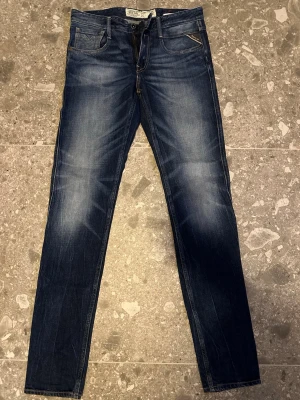Mörkblå slim fit jeans från Replay - Snygga mörkblå slim fit jeans från Replay med klassisk femficksdesign och subtila slitningar framtill och baktill. Jeansen har kontrastsömmar och är tillverkade i mjuk denim med en schysst tvättad look. Perfekta för dig som gillar en clean men ändå avslappnad stil.
