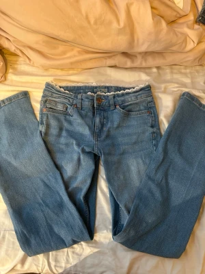 Bootcut lace jeans  - Säljer ett par ljusblå jeans köpte från Kappahl med snygg spetskant i midjan som är påsydd av mig. Klassisk femficksmodell, utsvängda ben och detaljer i kopparfärg. Perfekta för dig som vill ha en unik twist på dina jeans!