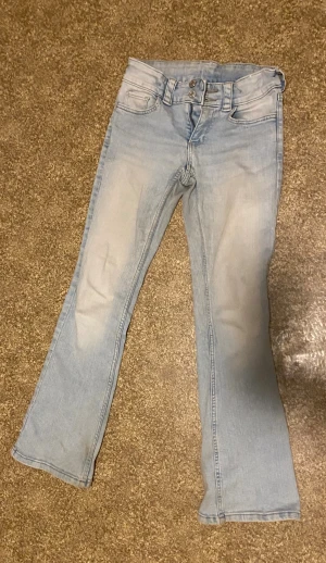 Lowrise bootcut jeans från H&M - Säljer ett par ljusblå bootcut jeans med dubbla knappar i midjan och fem fickor. Storlek 158. De sitter jättefint, men säljer eftersom de blivit för små. De lite smutsiga längst ner på benen, men inget som stör. Kom gärna med prisförslag!