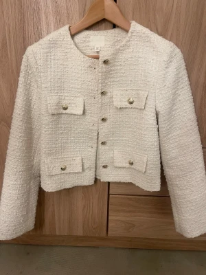 Vit tweed kavaj med guldknappar - Stilren vit kavaj i tweed med fyra fickor framtill och dekorativa guldknappar. Kort, boxig passform och rund halsringning. Perfekt för att lyfta vilken outfit som helst. Från hm i storlek xs. 