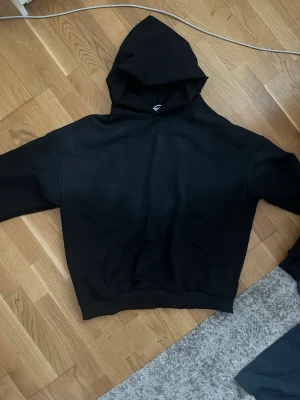 Svart hoodie Acne Studios Stockholm - Säljer en svart hoodie från Acne Studios med stor huva och tryck på ryggen där det står 'Acne Studios STOCKHOLM 1996'. Hoodien har ribbade muddar och en klassisk, avslappnad passform. Perfekt för dig som gillar streetwear och enkel stil.