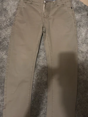 Beige chinos med raka ben - Snygga beige chinos med klassisk passform och raka ben. Byxorna har bälteshällor, knappgylf och fickor både fram och bak. Perfekta för en clean och stilren look. Materialet känns mjukt och bekvämt, troligen bomull eller bomullsblandning.