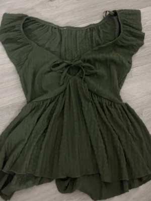 Grön omlottopp med volang och knyt - Supersöt mörkgrön topp med omlottdetalj och volangkant. Toppen har en snygg knytning framtill och är gjord i ett mjukt, strukturerat tyg,Perfekt att styla med jeans eller kjol ❤️
