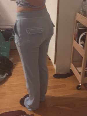 Ljusblå velour mjukisbyxor Juicy Coutoure - Säljer ett par ljusblå mjukisbyxor i mjuk velour från Juicy med bred resår i midjan och fickor både fram och bak. Byxorna har raka ben och en chill vibe, perfekta för att hänga hemma eller dra till kompisar i. Snygga detaljer med ficklock bak.