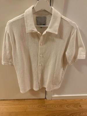 Vit kortärmad skjorta med knappar - Stilren vit skjorta med korta ärmar och klassisk krage. Skjortan har knappar framtill och är gjord i ett mjukt, strukturerat material som ger en avslappnad känsla. Perfekt för dig som gillar enkel och clean stil.