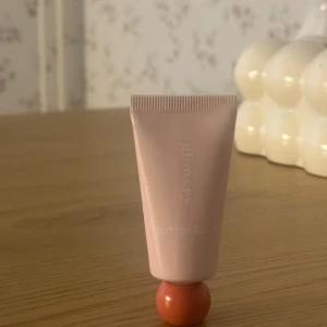 Glowery Butter Balm cream - Glowery  i en ljusrosa tub med en unik rund, orange botten. Tuben är smidig att ta med och har en modern design. Perfekt för att återfukta och ge glow 