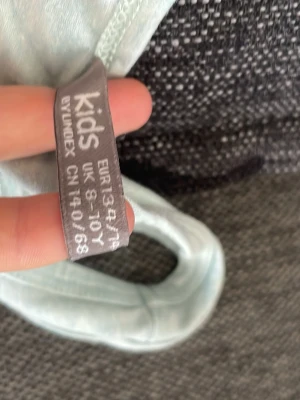 Ljusblå linnetopp från Lindex Kids - Säljer en ljusblå ärmlös linnetopp från Lindex Kids. Toppen har enkel design med rund halsringning och är tillverkad i mjuk bomull, perfekt för varma dagar eller som lager under andra plagg.