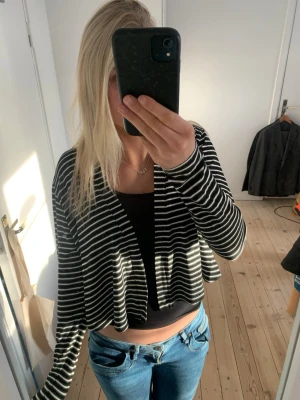 Svartvit randig croppad kofta från Marimekko - Säljer en svartvit randig croppad kofta från Marimekko med långa ärmar och öppen framtill. Koftan har tunnt, mjukt material (viskos)  och en avslappnad passform som passar perfekt till jeans eller kjol. Enkel och stilren design som funkar till många olika looks.