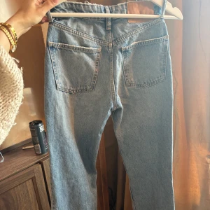Blå jeans från Zara - Säljer ett par blå straight jeans från Zara med midrise midja. Jeansen har klassiska fem fickor, egengjorda hål på framsidan och stora bakfickor. Tillverkade i kraftig denim med vintage tvättad look och knappgylf.